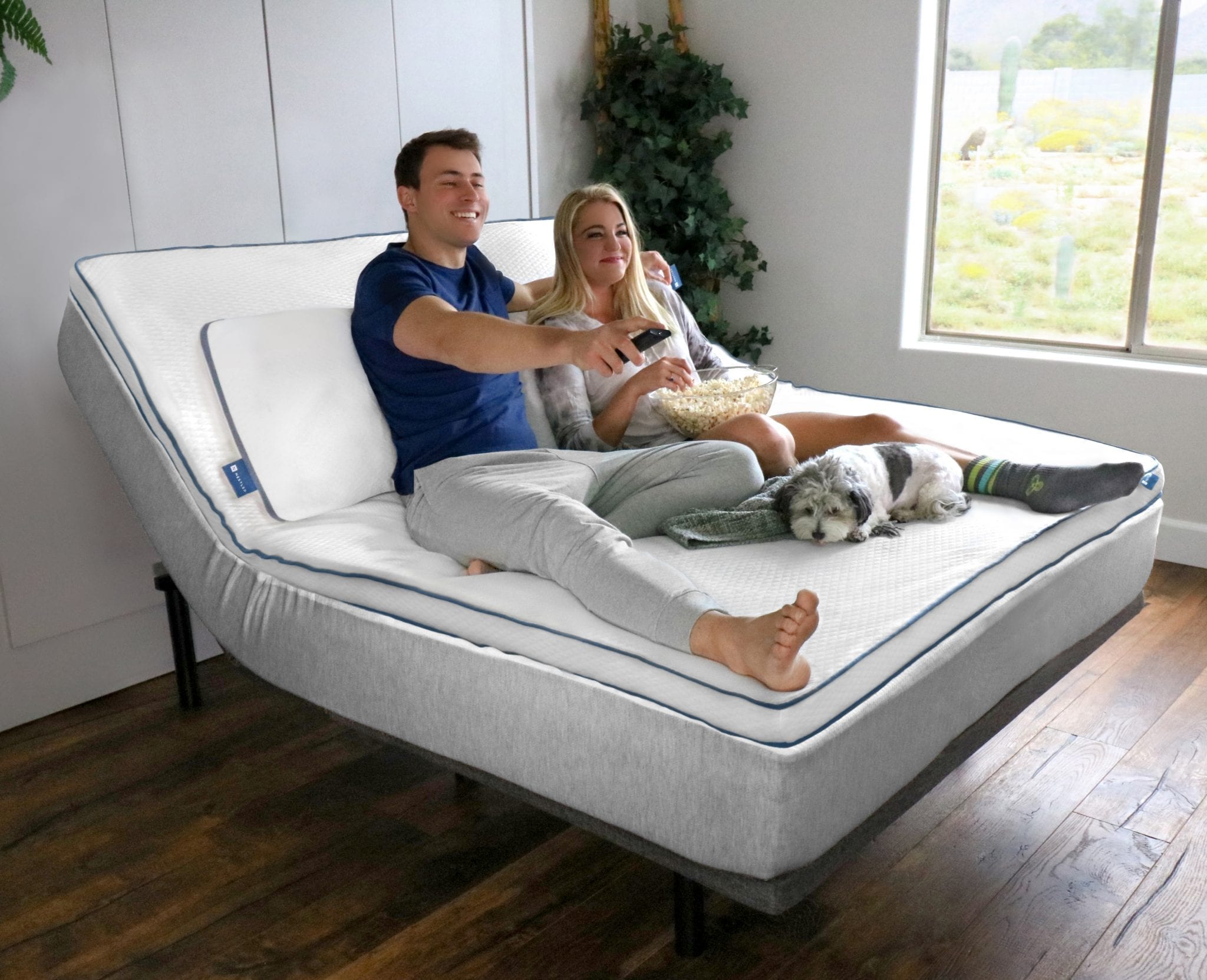 A couple happily watching TV on their Nestled topper and motion base with their cute dog.