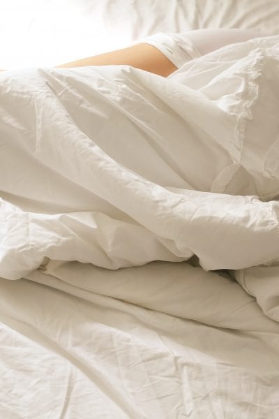 Person sleeping on side under white blanket.