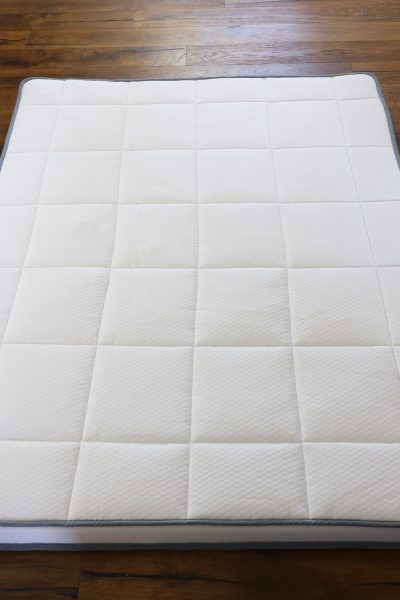 A Naturally Nestled mattress topper with a white cover resting on a dark hardwood floor
