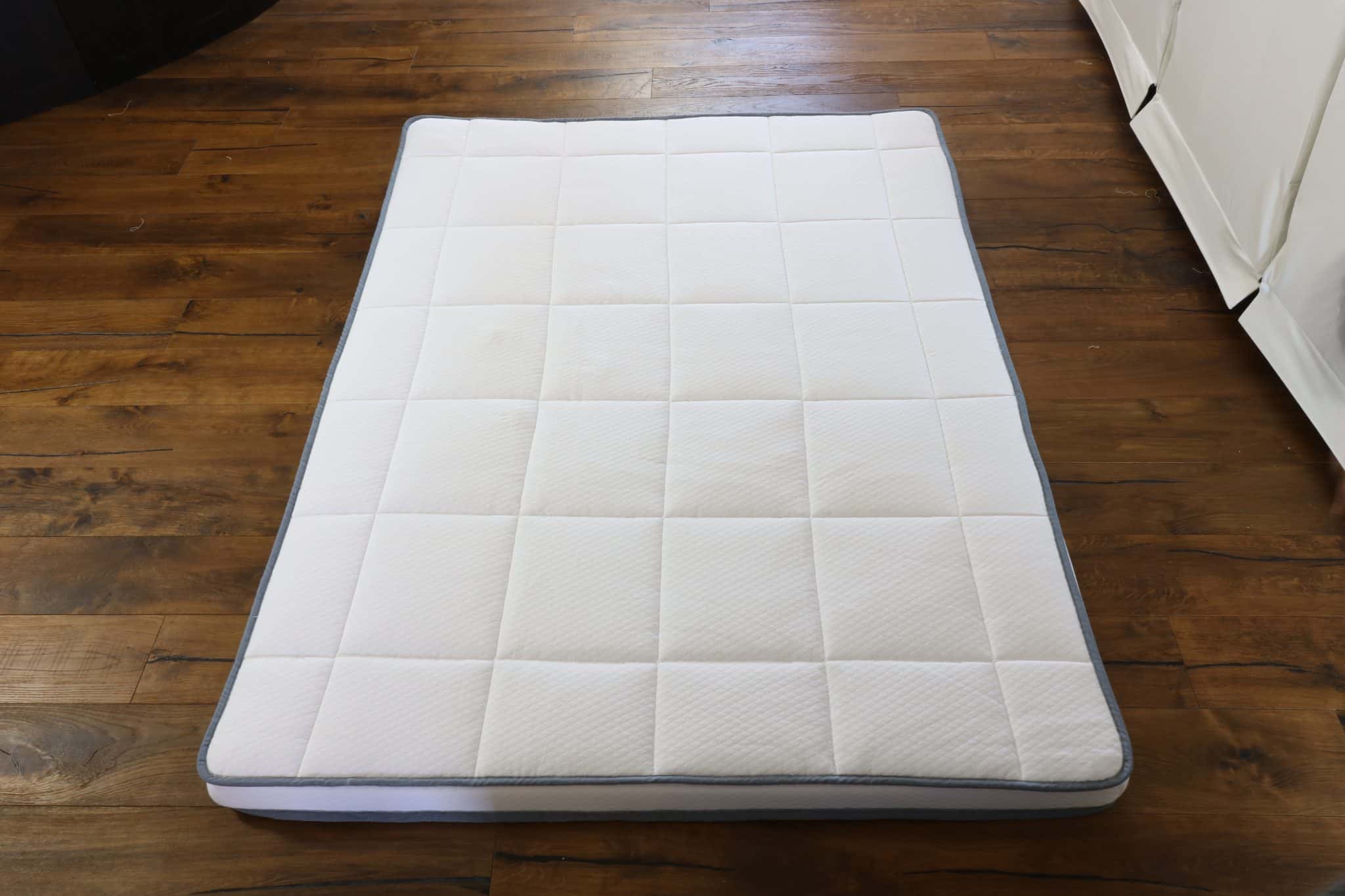 A Naturally Nestled mattress topper with a white cover resting on a dark hardwood floor