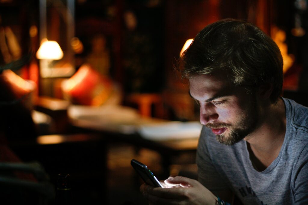 A man using a smartphone in a dimly lit room at night