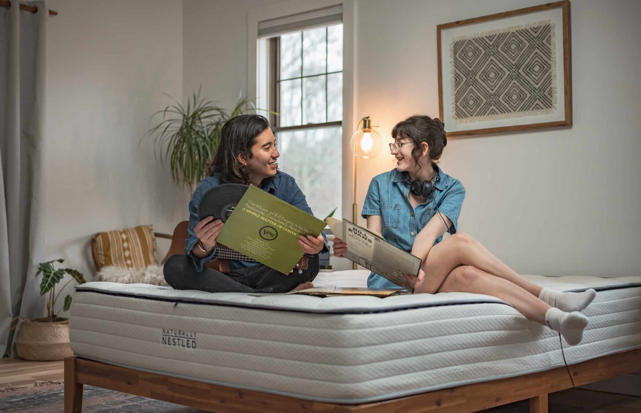 A couple looking at music records while sitting on a bare Naturally Nestled mattress