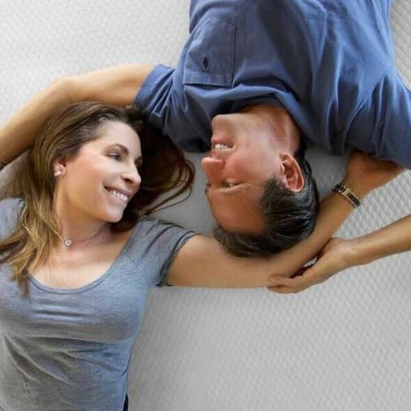 A man and woman smile at each other while laying on an eco-friendly mattress topper.
