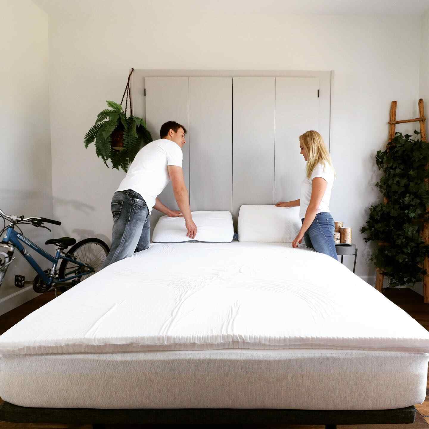 A man and a woman arrange the eco-friendly pillows on their eco-friendly mattress topper.