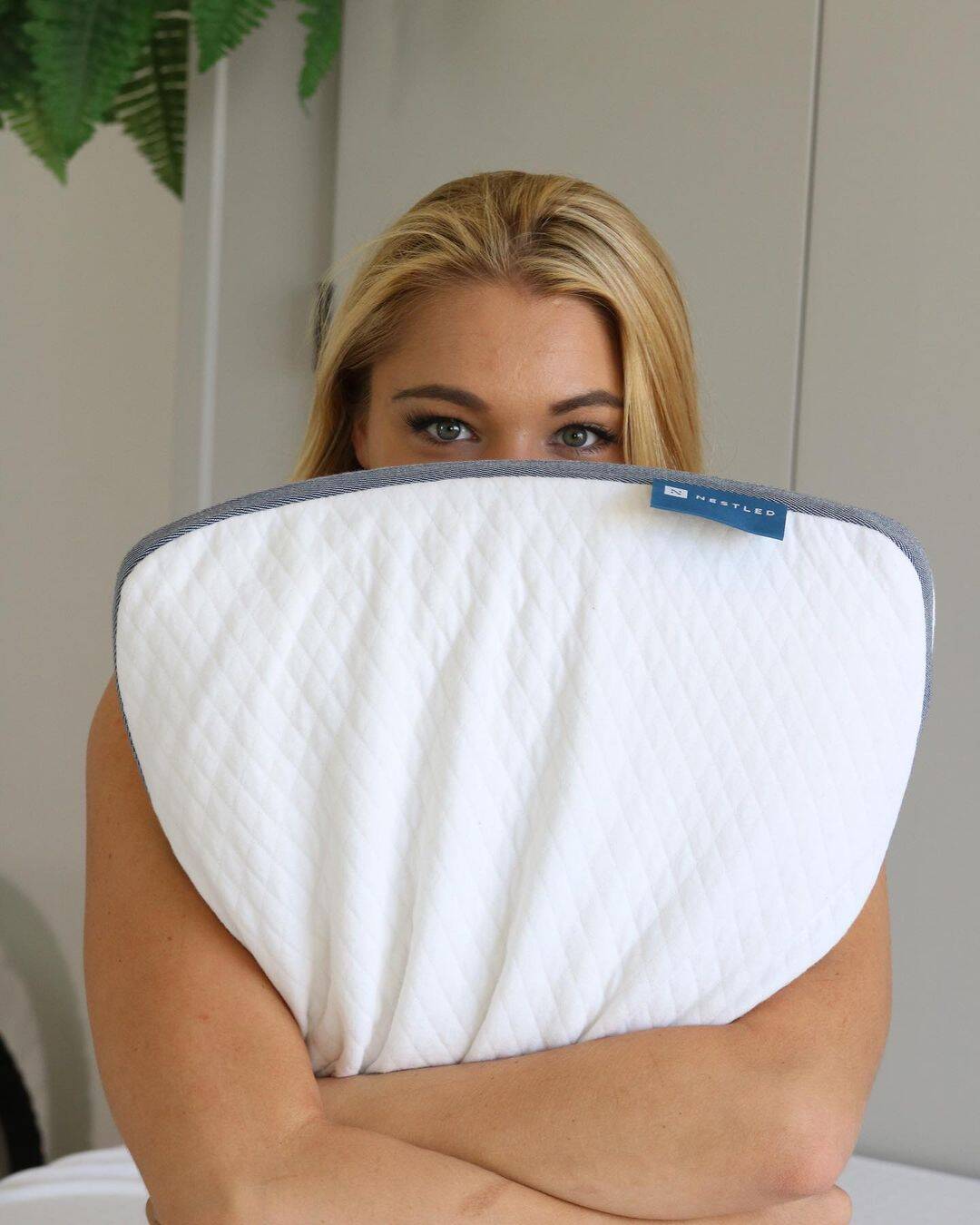 A woman holds an eco-friendly pillow in front of her face.
