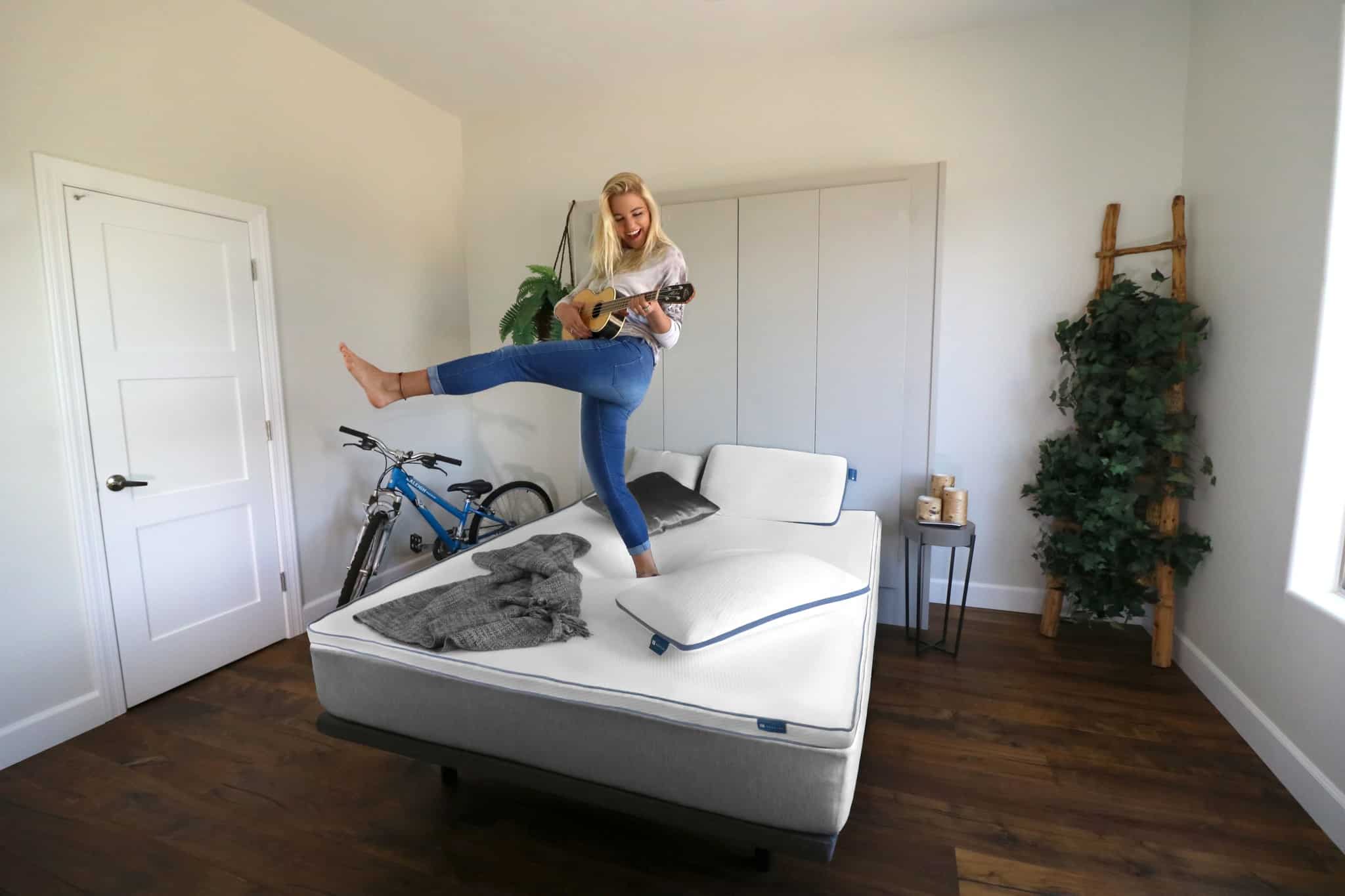 A woman dancing and playing a ukelele on the most durable mattress from Naturally Nestled