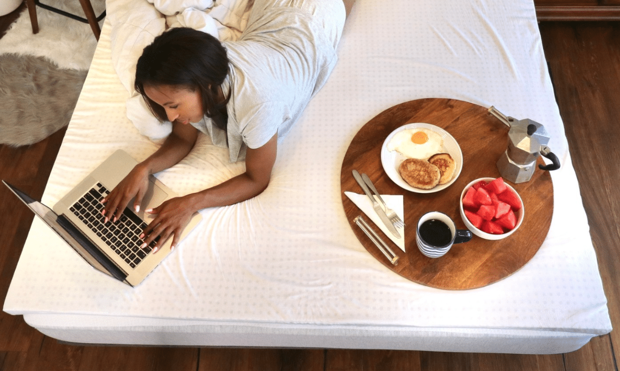 A woman working on her laptop and eating breakfast in bed on eco-friendly bedding