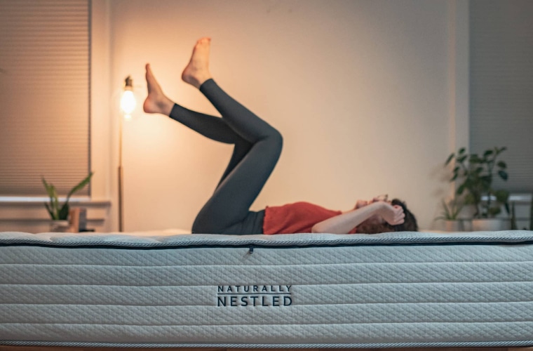 Woman lying on a mattress with a bedframe kicking both of her feet in the air