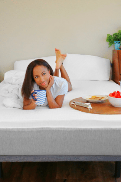A woman lying on a Naturally Nestled mattress with a cup of coffee and breakfast on a tray