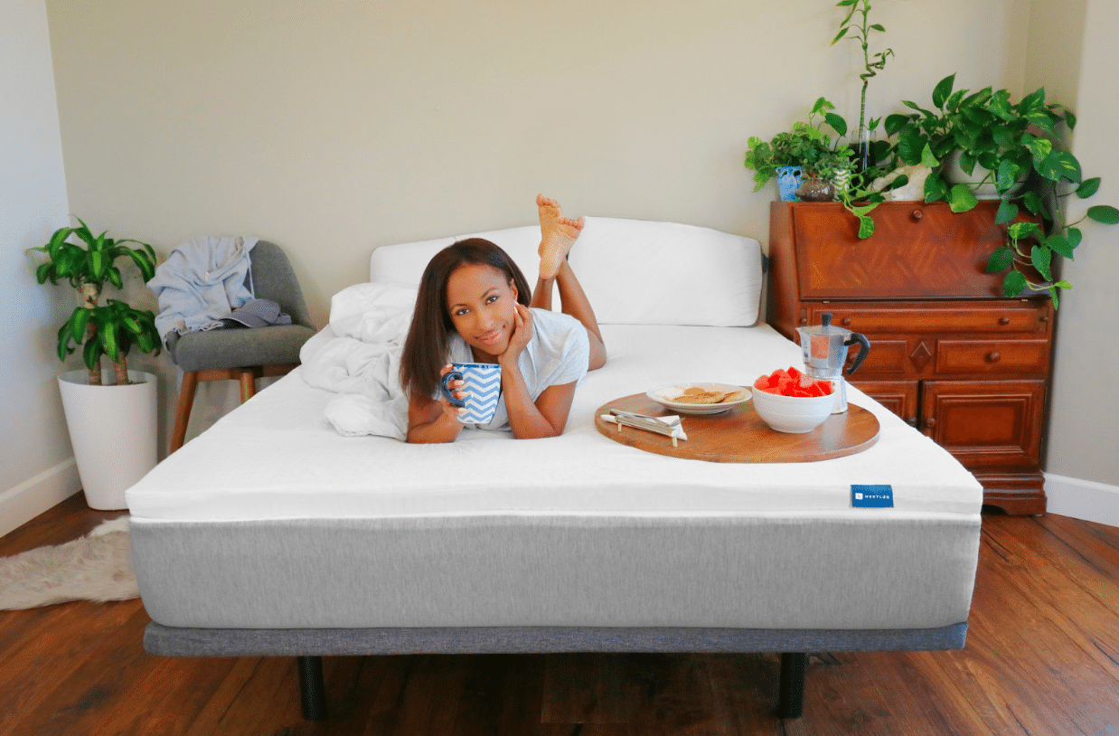A woman lying on a Naturally Nestled mattress with a cup of coffee and breakfast on a tray