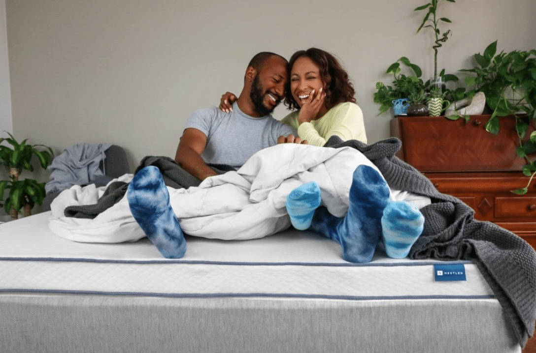 A couple sits comfortably on an eco-latex mattress topper from Naturally Nestled