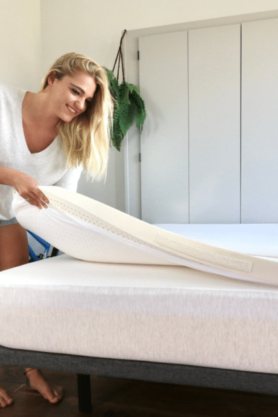 A woman placing a thick mattress topper from Naturally Nestled on top of an organic mattress