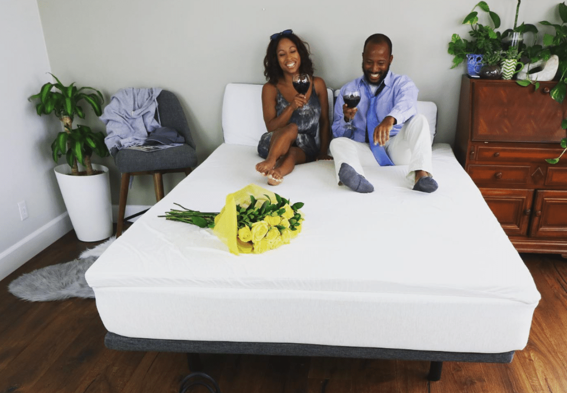 A man and a woman on a naturally nestled mattress with flowers after learning how to get the sweat smell out of a mattress