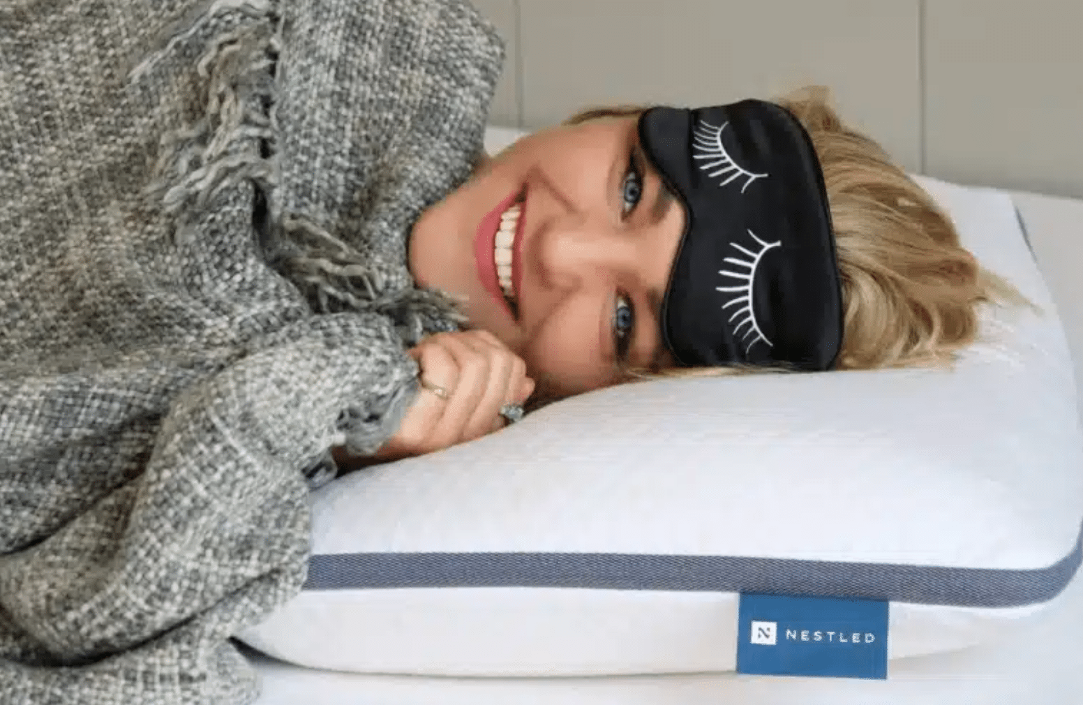  Girl lying on a Naturally Nestled pillow and mattress on a bed frame while laying under a gray blanket and wearing a sleep mask on her forehead
