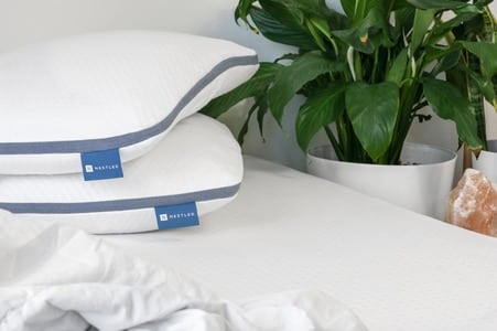 A stack of natural pillows on a mattress next to a green plant