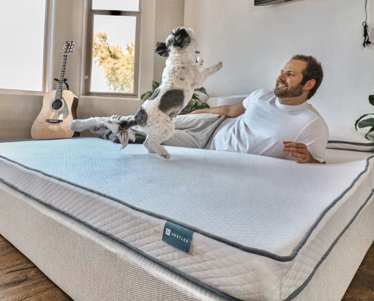 A smiling man and his dog are on his latex mattress in the bedroom