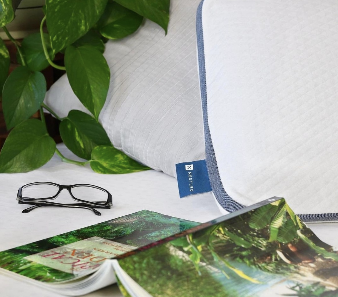 A Naturally Nestled pillow next to a book and reading glasses