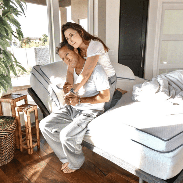 Couple sits on top of a soft mattress topper in a sunshine-filled bedroom